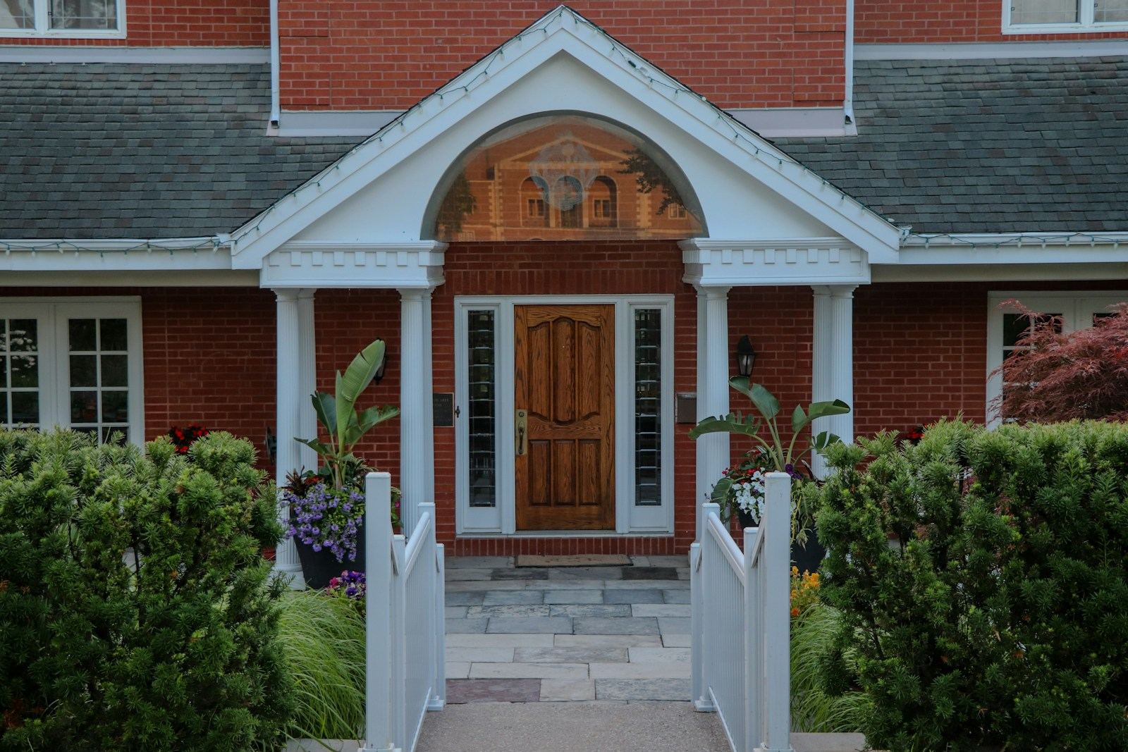 Front entrance of a well kept brick home with a covered portico, landscaping, and a paver walk