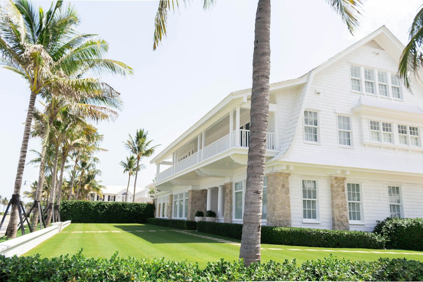 White two story coastal Florida home with palm trees and a trimmed hedge on a clear day